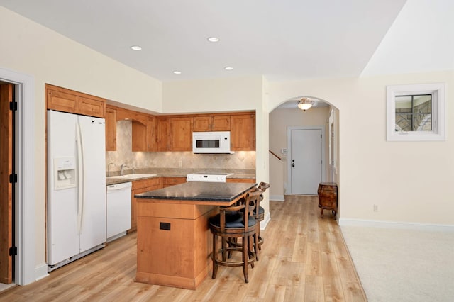 kitchen featuring white appliances, light wood-type flooring, a kitchen island, a kitchen bar, and tasteful backsplash