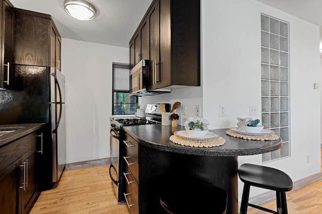 kitchen featuring dark brown cabinets, a breakfast bar area, light hardwood / wood-style flooring, fridge, and black range with gas stovetop