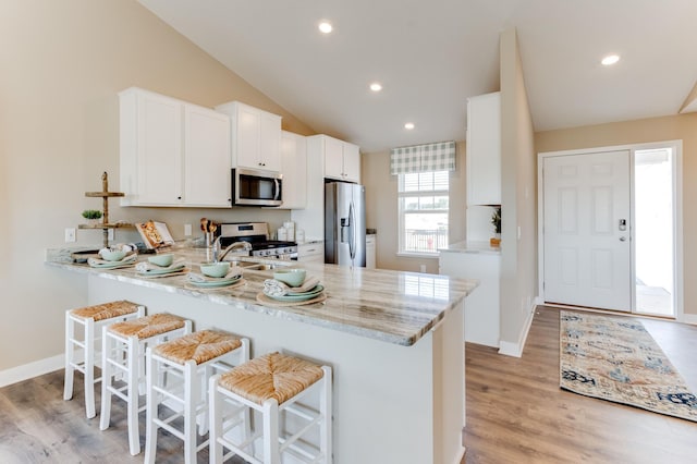 kitchen with lofted ceiling, kitchen peninsula, a kitchen bar, white cabinetry, and appliances with stainless steel finishes