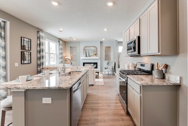 kitchen with appliances with stainless steel finishes, a textured ceiling, a kitchen island with sink, and a breakfast bar area