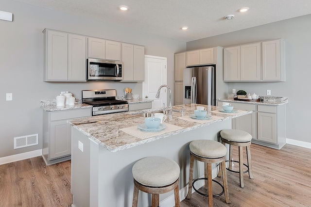 kitchen with sink, a kitchen island with sink, stainless steel appliances, and a textured ceiling