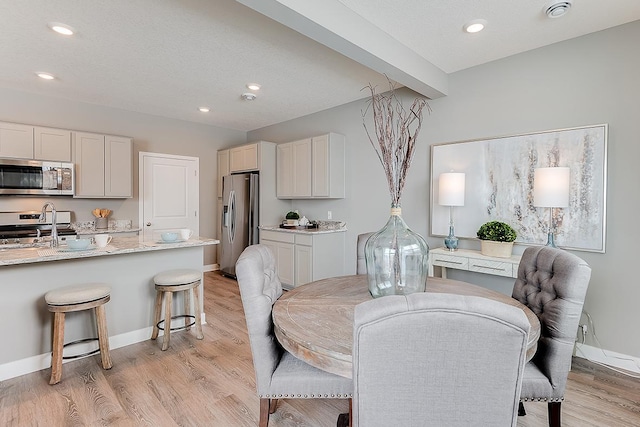 dining room with sink, beamed ceiling, and light hardwood / wood-style flooring