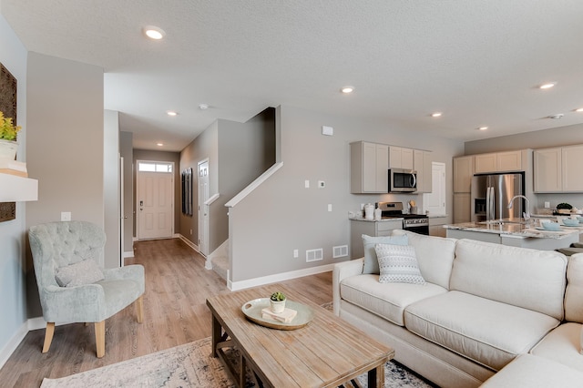 living room featuring sink, a textured ceiling, and light wood-type flooring