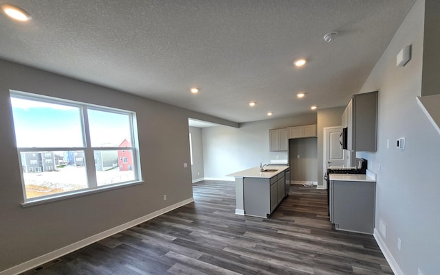 kitchen featuring a textured ceiling, a kitchen island with sink, dark wood-type flooring, and gray cabinetry