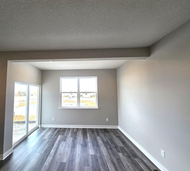 empty room with beam ceiling, a textured ceiling, and dark hardwood / wood-style flooring