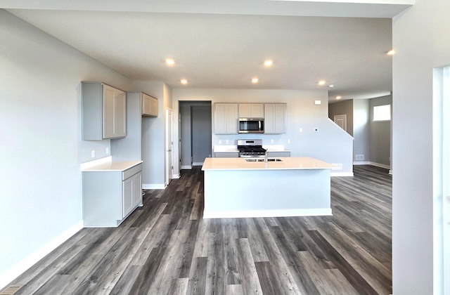 kitchen with gray cabinetry, appliances with stainless steel finishes, sink, dark hardwood / wood-style flooring, and a center island with sink