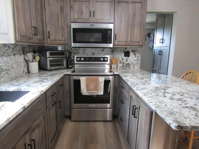 kitchen featuring a breakfast bar, appliances with stainless steel finishes, light stone countertops, and dark wood-type flooring