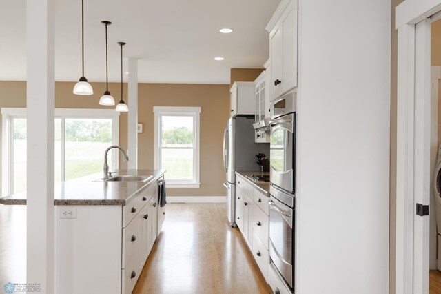 16305 57th St SE, Kindred, ND 58051 - kitchen featuring a sink, white cabinets, a center island with sink, appliances with stainless steel finishes, and decorative light fixtures