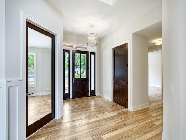 foyer featuring light wood-style floors, a chandelier, baseboards, and a healthy amount of sunlight