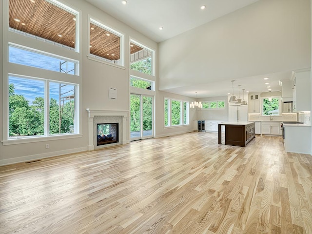 unfurnished living room with light wood-style flooring, a high ceiling, a notable chandelier, baseboards, and a glass covered fireplace