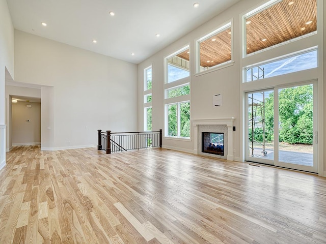 unfurnished living room with a premium fireplace, light wood-style flooring, a high ceiling, and baseboards