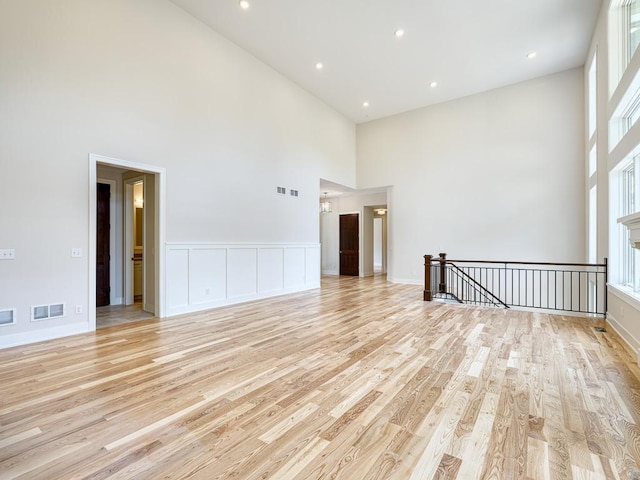empty room with a towering ceiling, light wood-style flooring, and visible vents