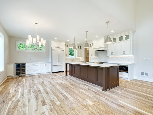 kitchen with hanging light fixtures, white cabinetry, paneled built in fridge, beverage cooler, and a kitchen island with sink