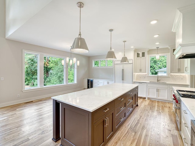 kitchen with hanging light fixtures, backsplash, premium appliances, white cabinets, and light hardwood / wood-style floors