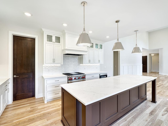 kitchen featuring stainless steel range, white cabinetry, a kitchen island, and light hardwood / wood-style floors