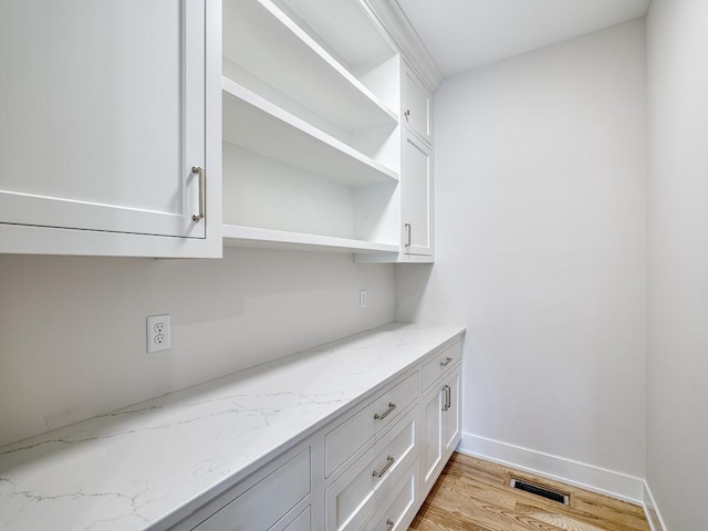 bar with white cabinetry, light hardwood / wood-style floors, and light stone counters