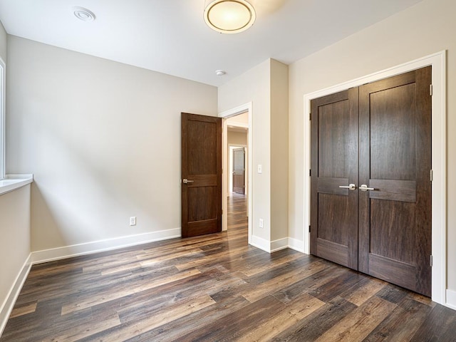 unfurnished bedroom with baseboards, dark wood-style flooring, and a closet