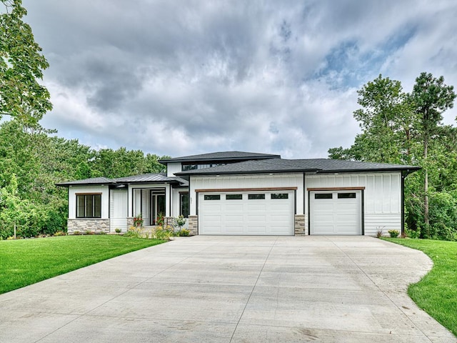 prairie-style house featuring board and batten siding, a garage, concrete driveway, stone siding, and a front lawn