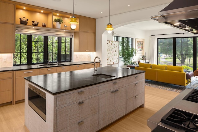 kitchen featuring built in microwave, ventilation hood, backsplash, sink, and a kitchen island with sink