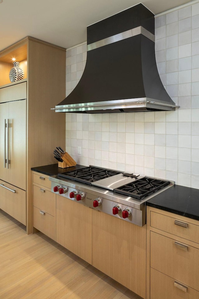 kitchen with light hardwood / wood-style flooring, stainless steel gas cooktop, tasteful backsplash, paneled refrigerator, and wall chimney exhaust hood