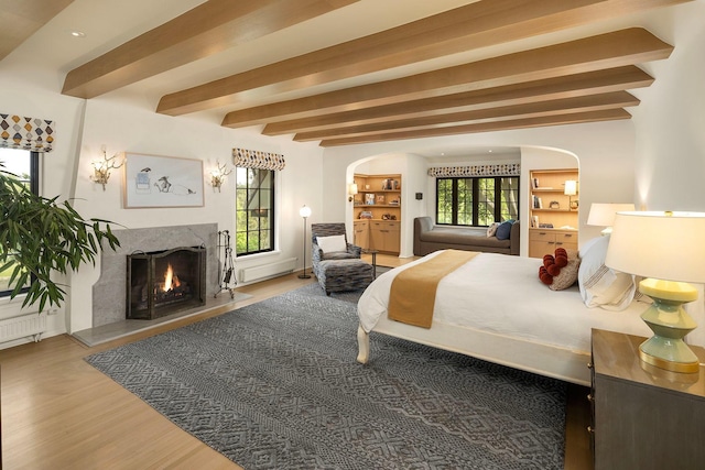 bedroom featuring beam ceiling, a fireplace, and wood-type flooring