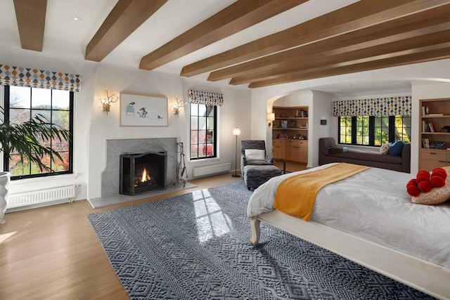 bedroom featuring a fireplace, radiator, hardwood / wood-style floors, beamed ceiling, and connected bathroom