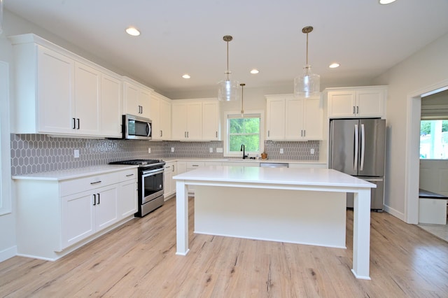 kitchen with white cabinetry, sink, stainless steel appliances, pendant lighting, and a kitchen island