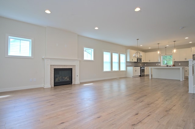 unfurnished living room with light wood-type flooring, baseboards, a glass covered fireplace, and recessed lighting