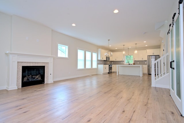 unfurnished living room featuring recessed lighting, stairway, a barn door, a sink, and light wood-type flooring