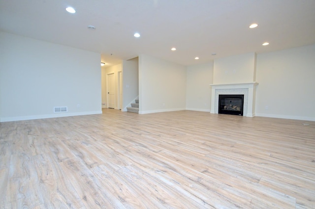 unfurnished living room featuring light wood-type flooring, recessed lighting, visible vents, and a glass covered fireplace