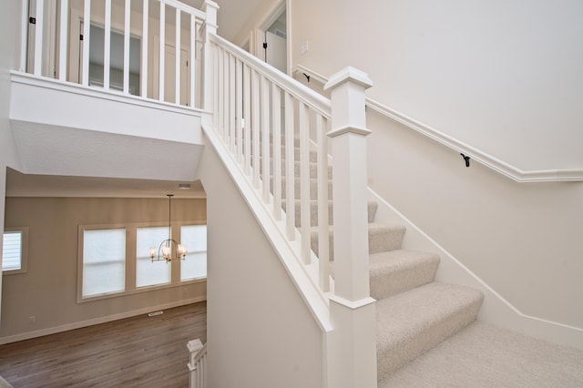 stairs featuring an inviting chandelier, a high ceiling, baseboards, and wood finished floors