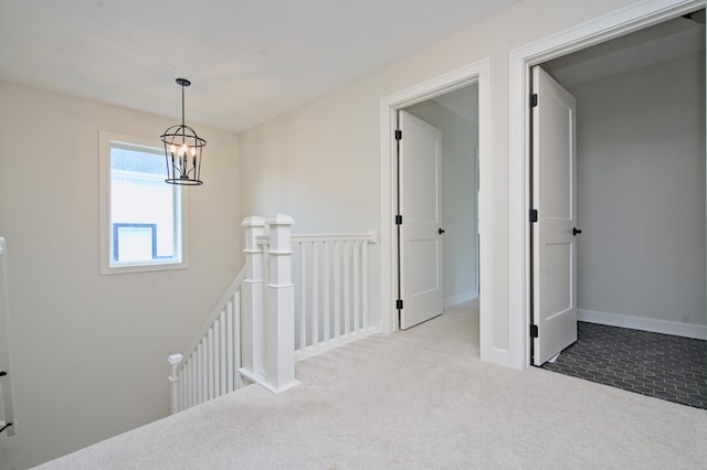 hallway featuring light carpet, baseboards, a notable chandelier, and an upstairs landing