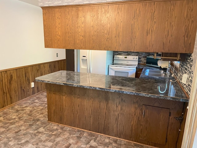 kitchen featuring white appliances, sink, kitchen peninsula, dark stone counters, and wooden walls