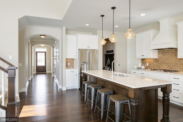 kitchen with a center island with sink, dark wood-type flooring, sink, decorative backsplash, and custom exhaust hood