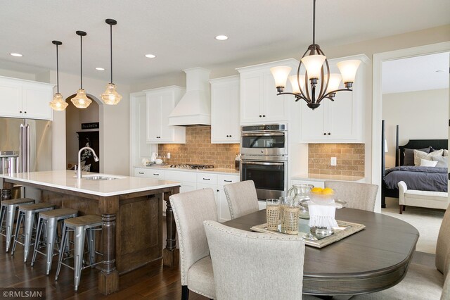 interior space featuring hanging light fixtures, premium range hood, decorative backsplash, and a kitchen island with sink