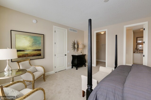 bedroom featuring a textured ceiling, light colored carpet, a walk in closet, and a closet