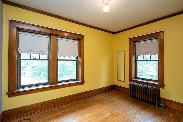 unfurnished room featuring light hardwood / wood-style floors, ornamental molding, radiator heating unit, and a wealth of natural light