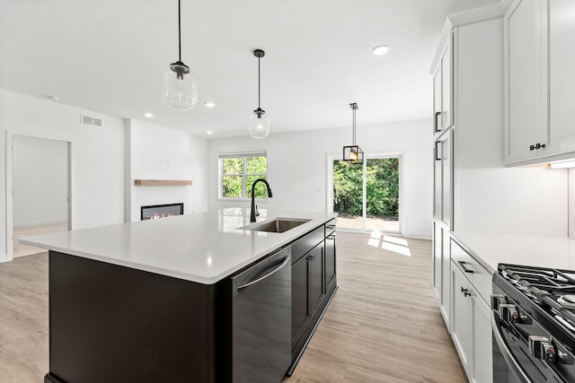 kitchen featuring sink, stainless steel dishwasher, decorative light fixtures, a center island with sink, and light hardwood / wood-style flooring