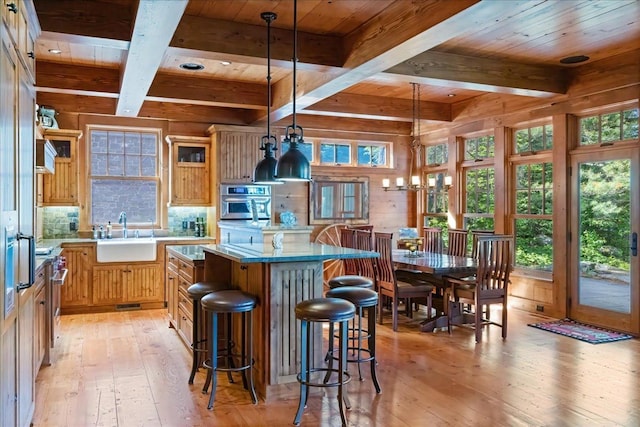 kitchen with a center island, sink, hanging light fixtures, stainless steel oven, and light wood-type flooring