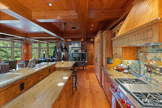 kitchen featuring decorative light fixtures, beam ceiling, a breakfast bar, light wood-type flooring, and light stone counters