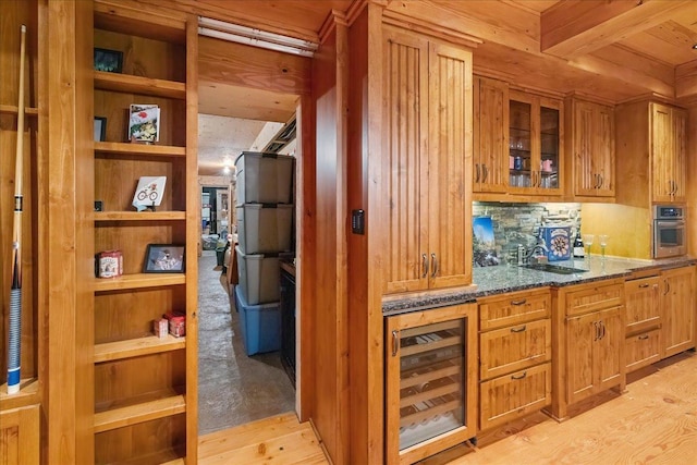 kitchen with wine cooler, dark stone counters, stainless steel oven, and light hardwood / wood-style flooring