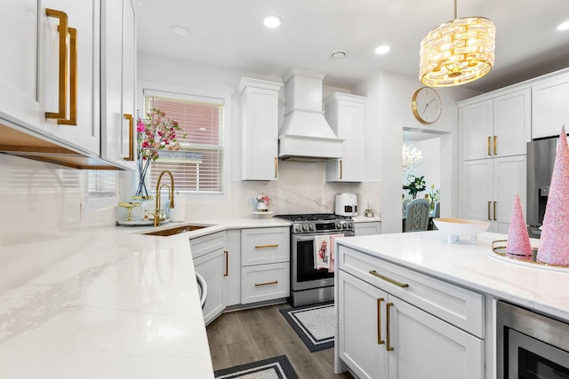 kitchen with appliances with stainless steel finishes, custom exhaust hood, sink, white cabinets, and hanging light fixtures