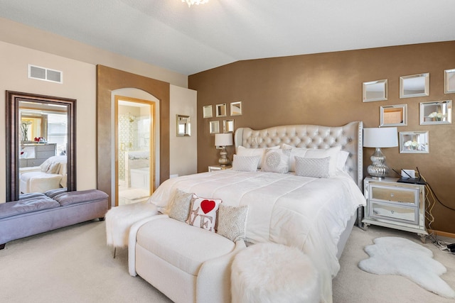 bedroom with ensuite bathroom, light carpet, and vaulted ceiling