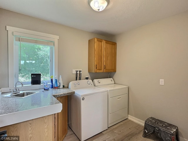 laundry area with a sink, baseboards, light wood-style floors, independent washer and dryer, and cabinet space