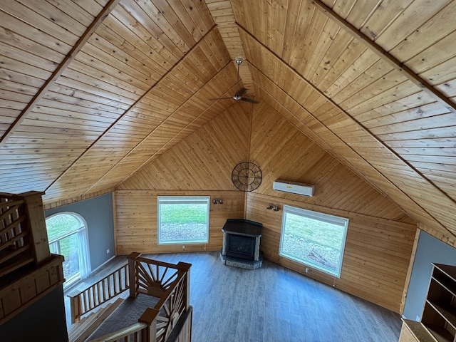 interior space with wood ceiling, lofted ceiling, a wood stove, wooden walls, and wood finished floors