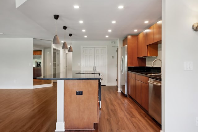 kitchen featuring appliances with stainless steel finishes, wood-type flooring, sink, a breakfast bar area, and hanging light fixtures