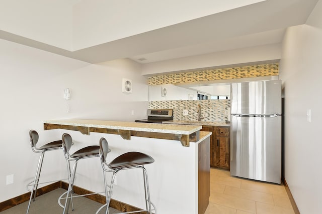 kitchen with sink, a breakfast bar area, stainless steel appliances, tasteful backsplash, and kitchen peninsula