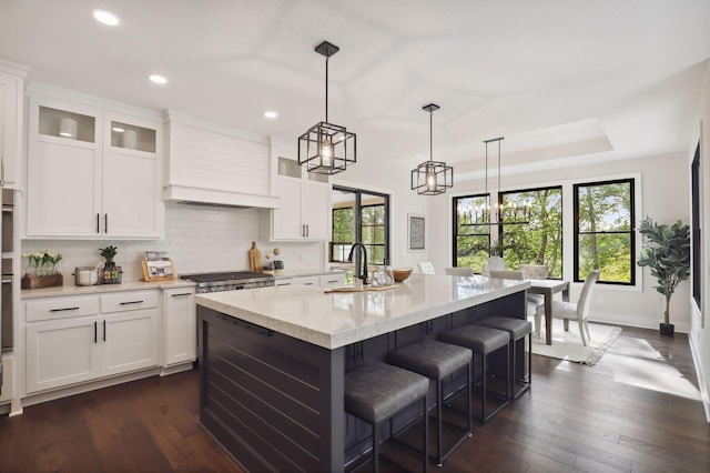 kitchen featuring a kitchen island with sink, dark hardwood / wood-style floors, hanging light fixtures, and a raised ceiling