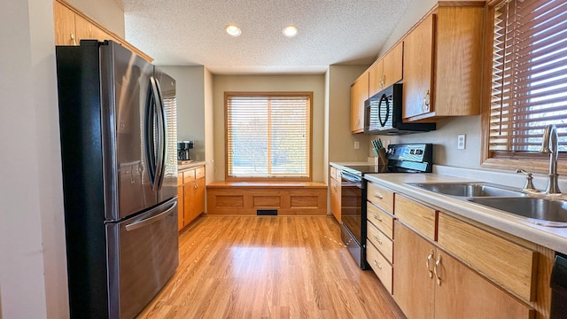 kitchen featuring a textured ceiling, black appliances, sink, and light wood-type flooring