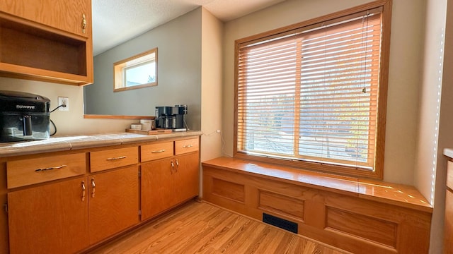 kitchen with tile countertops, a textured ceiling, light wood-type flooring, and a wealth of natural light